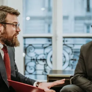 Deux hommes élégamment habillés discutent dans un salon raffiné. L